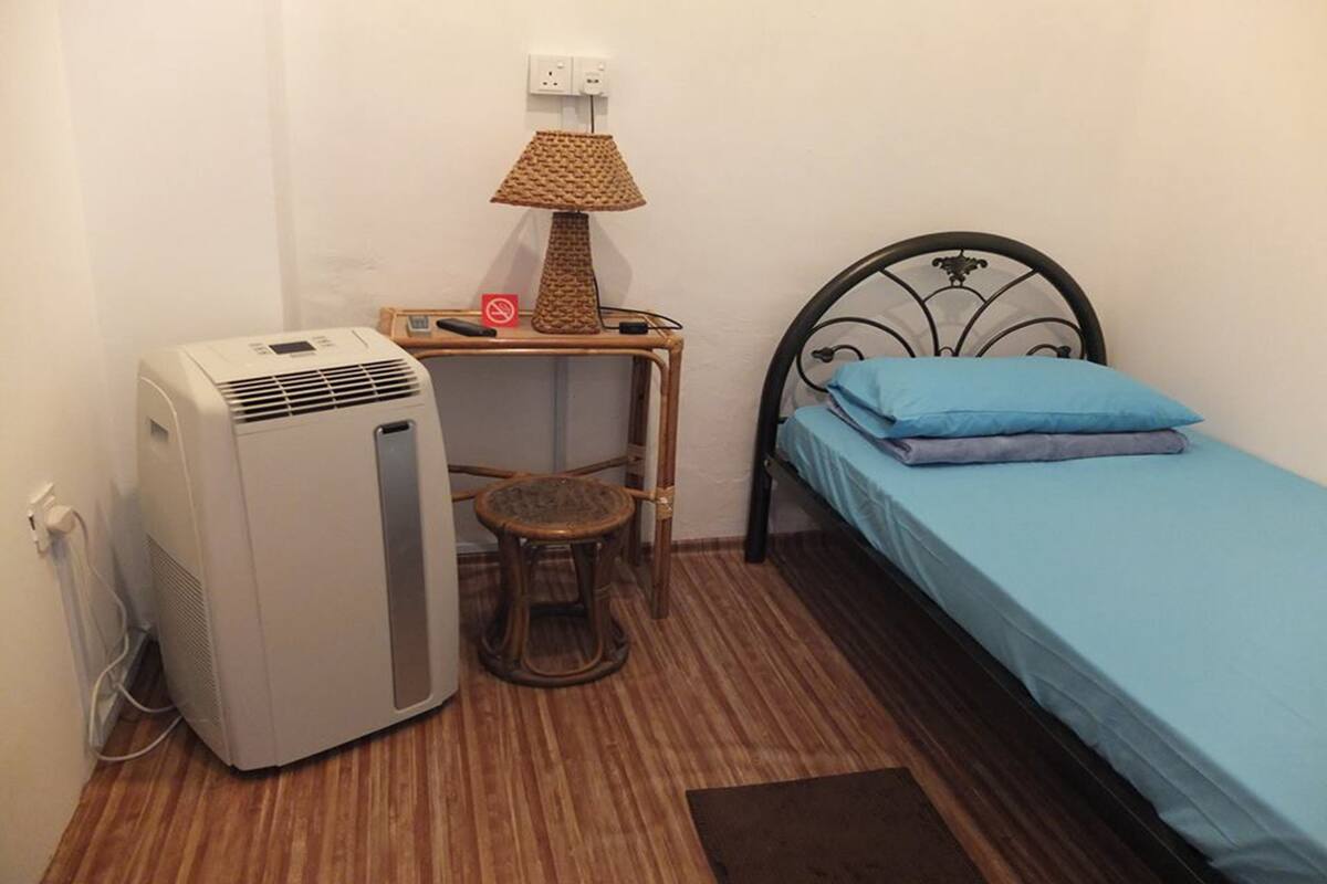 A small room with a bed, a heater, a stool, and a table with a lamp.