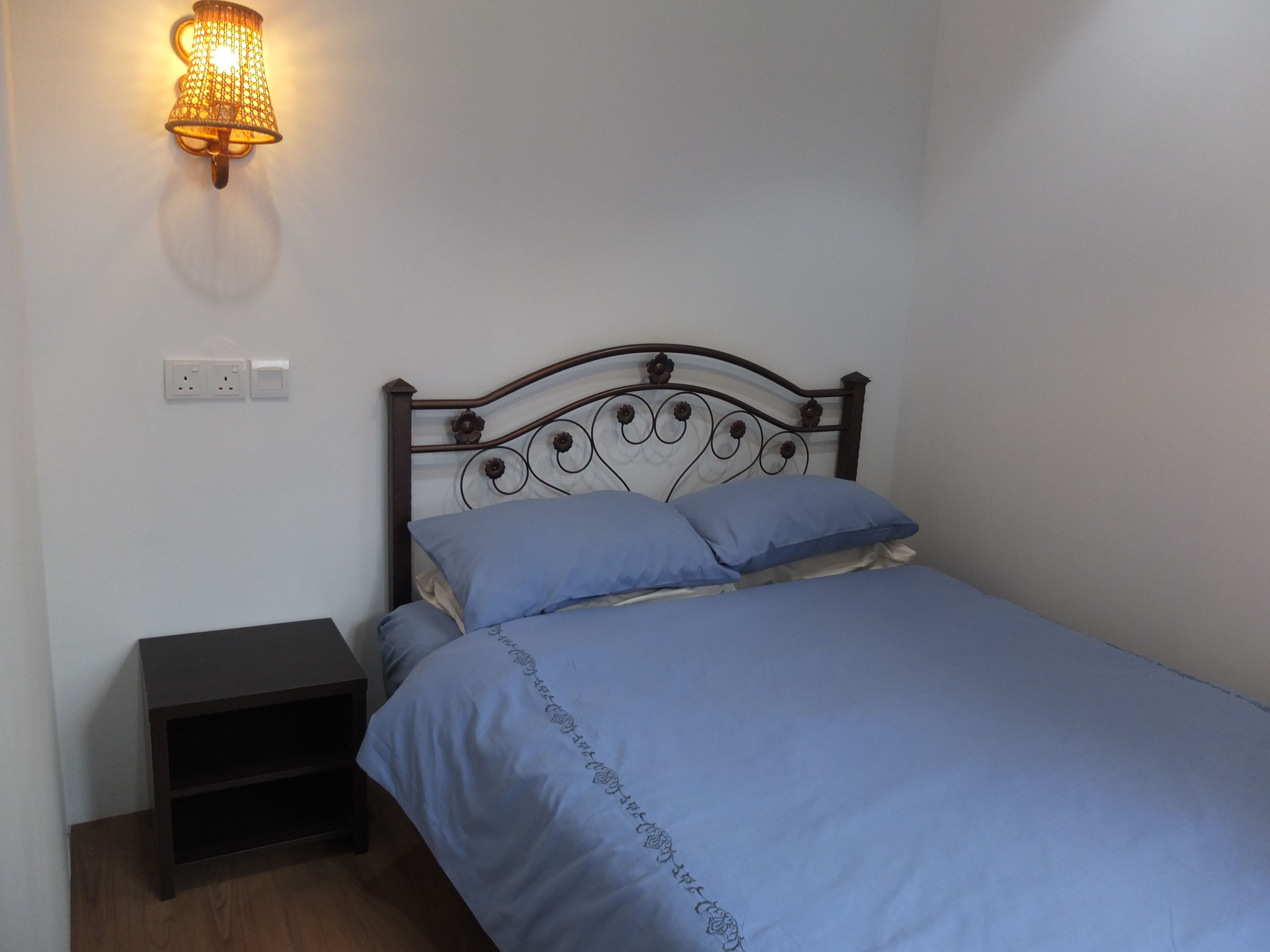 A single bed with a metal headboard, a bedside table, and a wall-mounted light fixture.