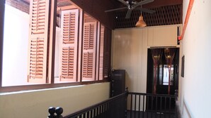 A staircase with a wooden railing, a ceiling fan, and a view of a building with wooden shutters. - Muntri House - Hostel (George Town)