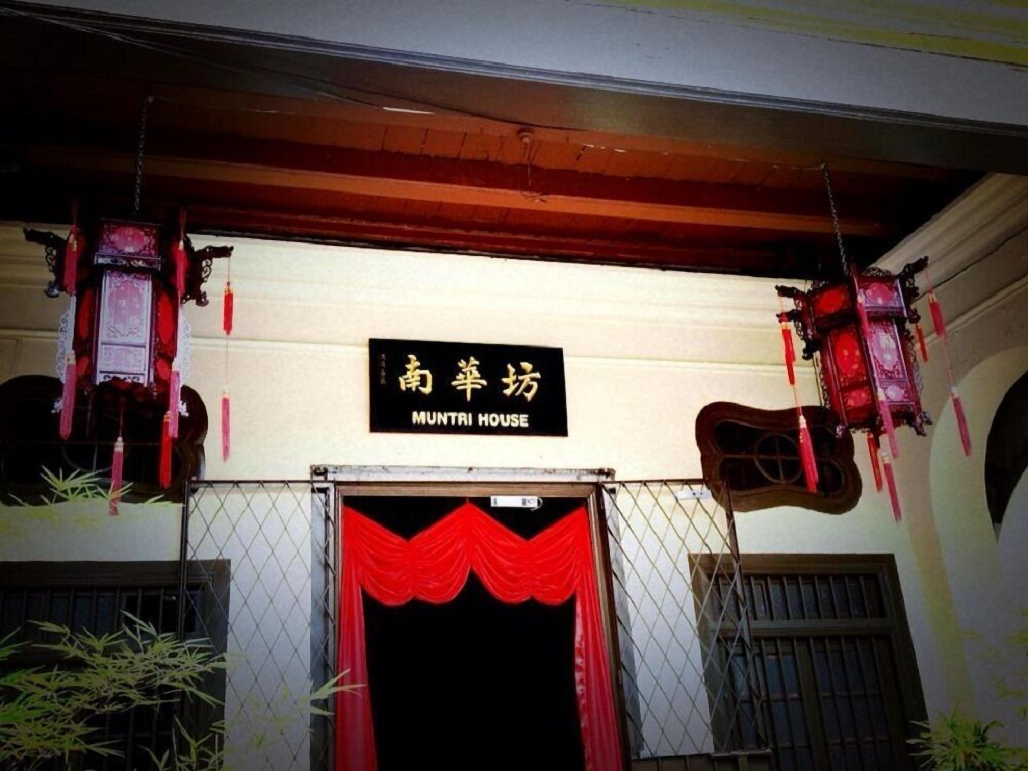 L'ingresso di un edificio con un cartello che riporta "MUNTRI HOUSE" e tradizionali lanterne rosse appese sopra.