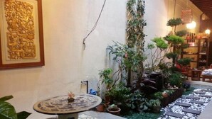 A courtyard with a tiled floor, a small table with a decorative top, and various potted plants. - Muntri House - Hostel (George Town)