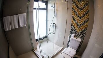Un bagno moderno con doccia a parete in vetro, un WC con decorazione in mosaico e un set di asciugamani bianchi appesi al muro.