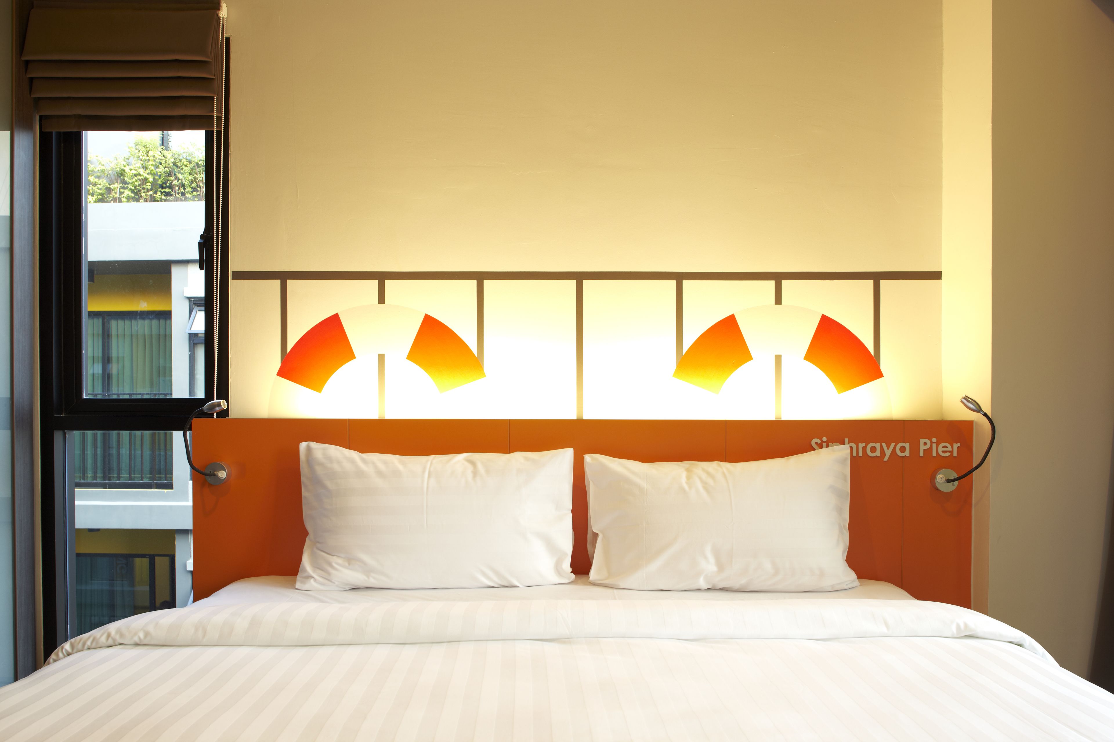 A hotel room with a bed, two pillows, a headboard, and a window with blinds.