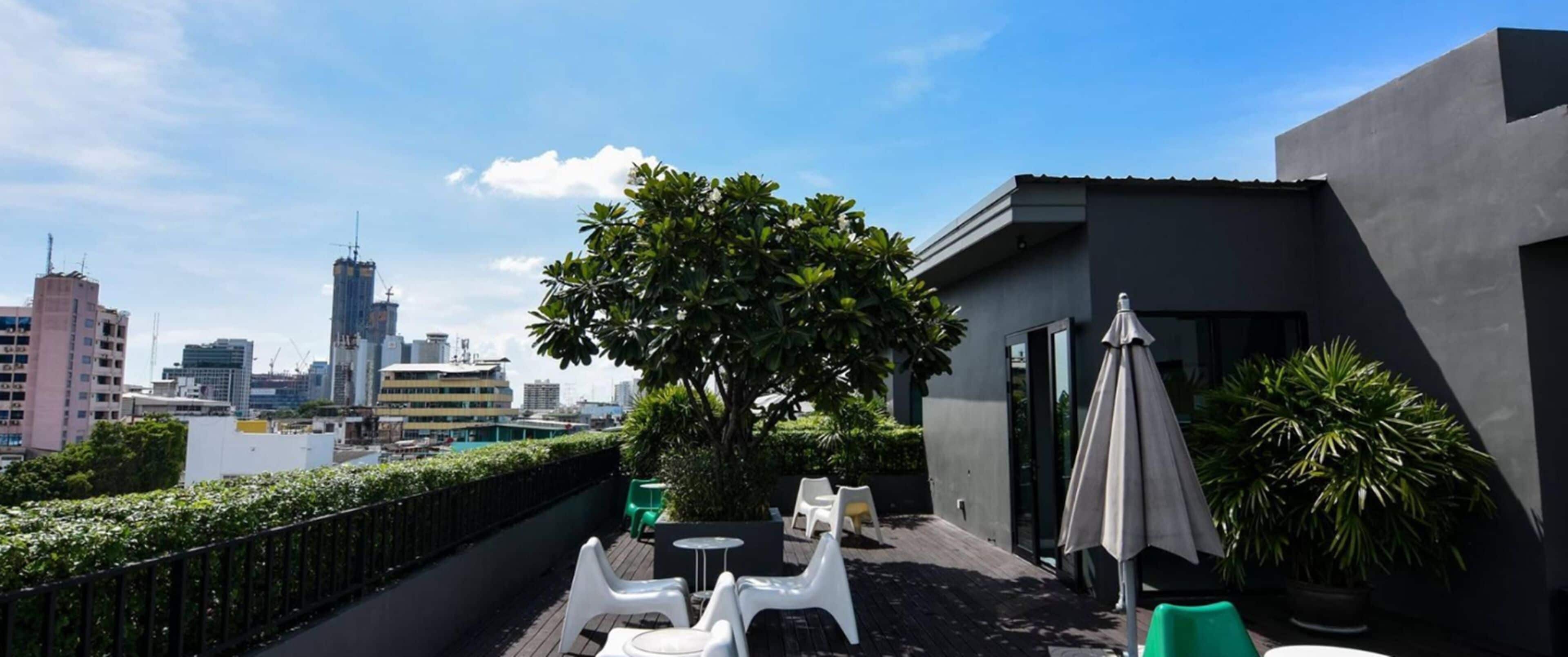 Eine Dachterrasse mit Außenbestuhlung, ein großer Baum und eine Skyline im Hintergrund.