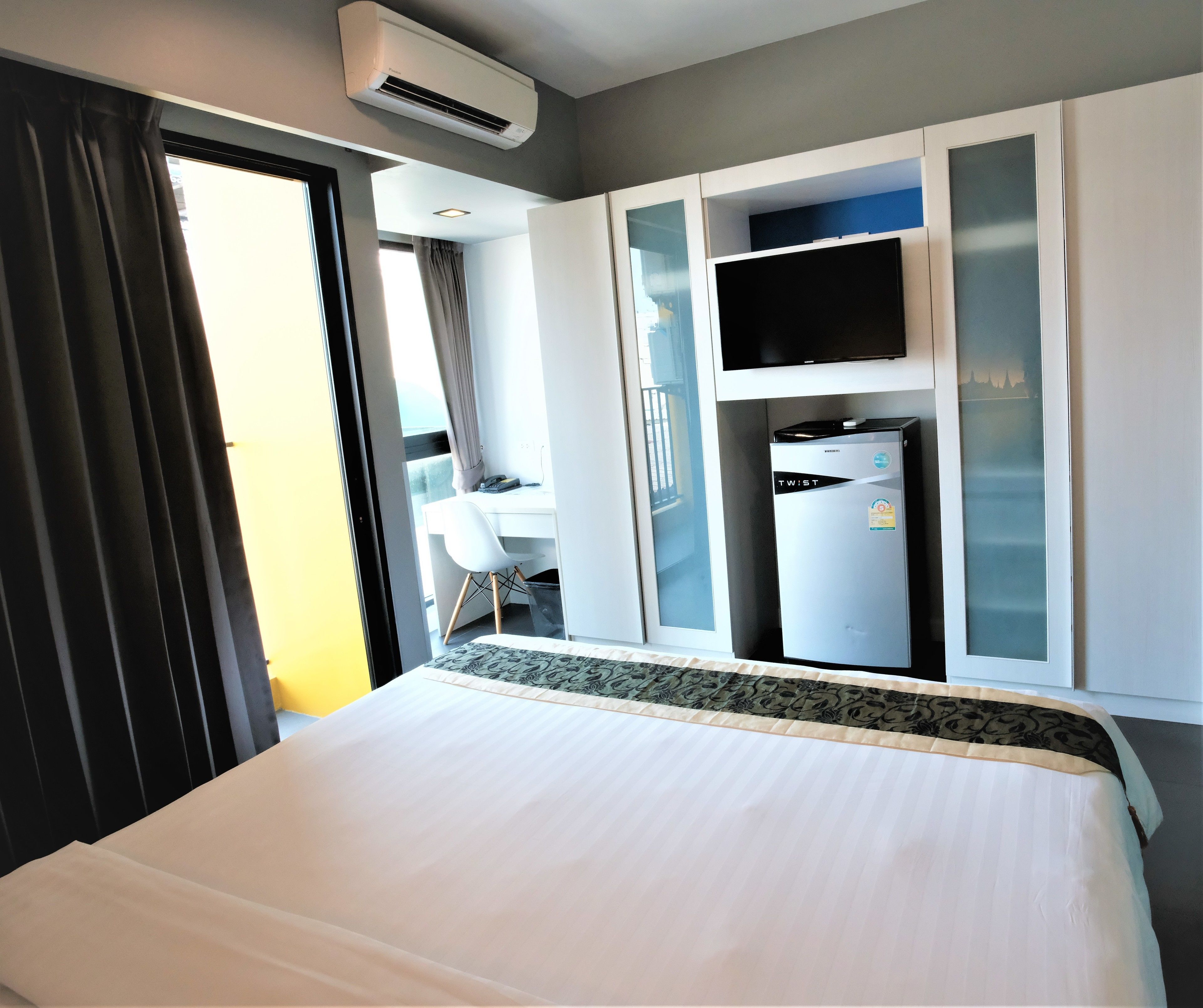 Una habitación de hotel con cama, escritorio, televisor y minibar.