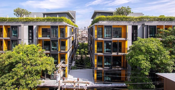 A modern building with multiple floors, featuring balconies with greenery, large windows, and a central courtyard.