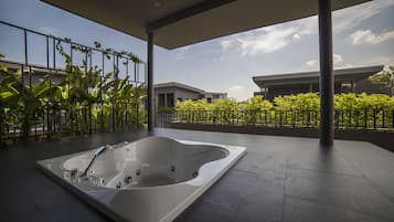 A modern outdoor spa area with a large hot tub, surrounded by a metal railing and lush greenery.