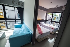 A modern hotel room with a large window, a blue sofa, two beds with white bedding, and a visible balcony.