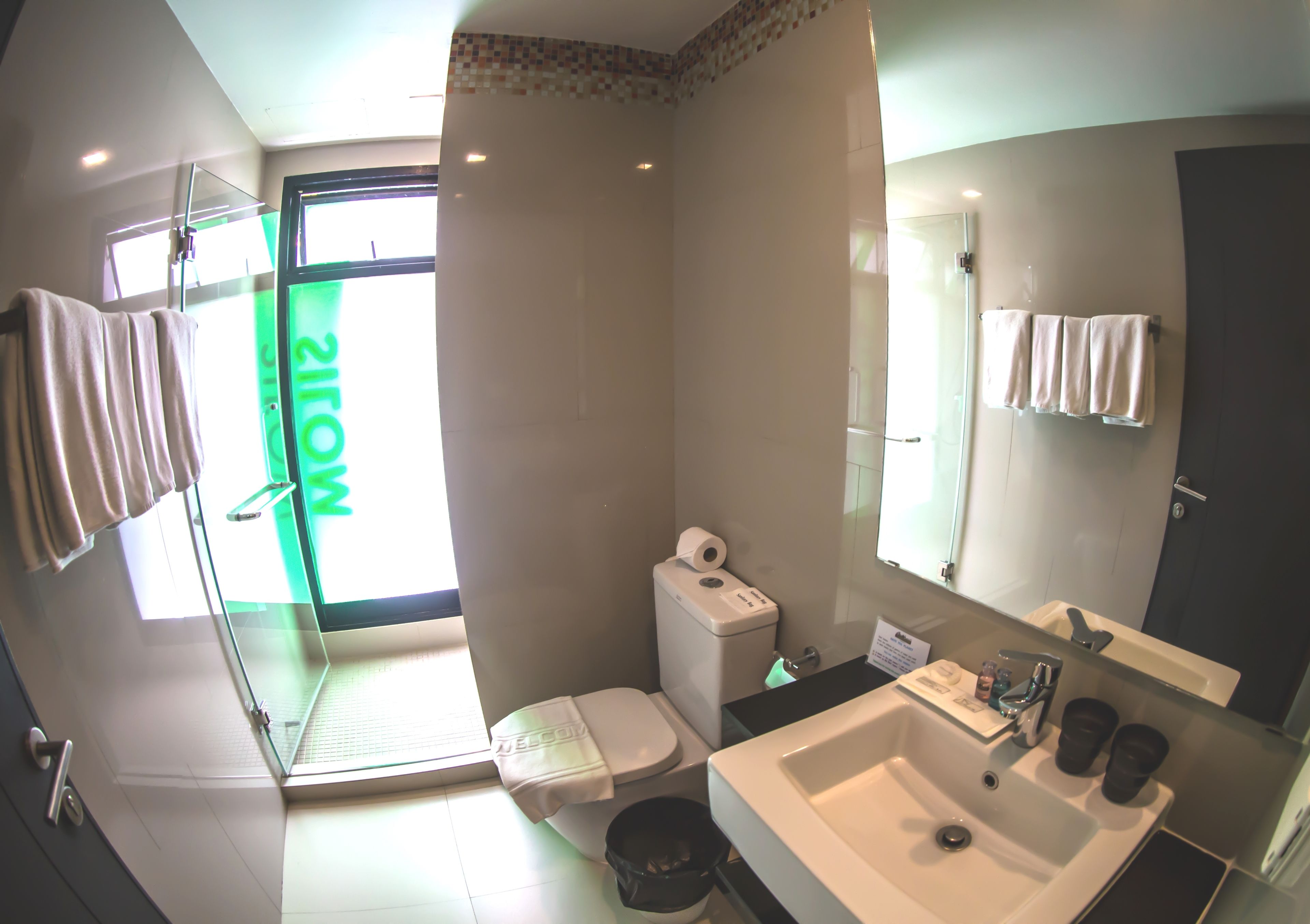 Un baño moderno con cabina de ducha de vidrio, inodoro, lavamanos con espejo y toallero.
