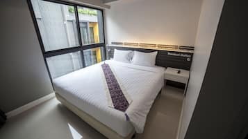 A modern hotel room with a large bed, a bedside table, a nightstand, and a view of the outside through a large window.