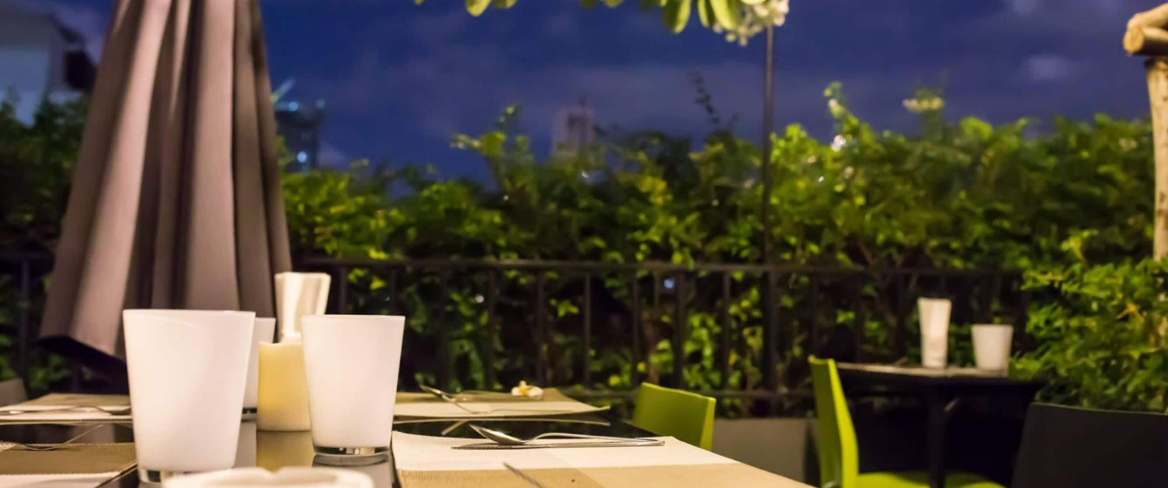 Un espacio de comedor al aire libre con mesas dispuestas para dos personas, con manteles blancos y candelabros.