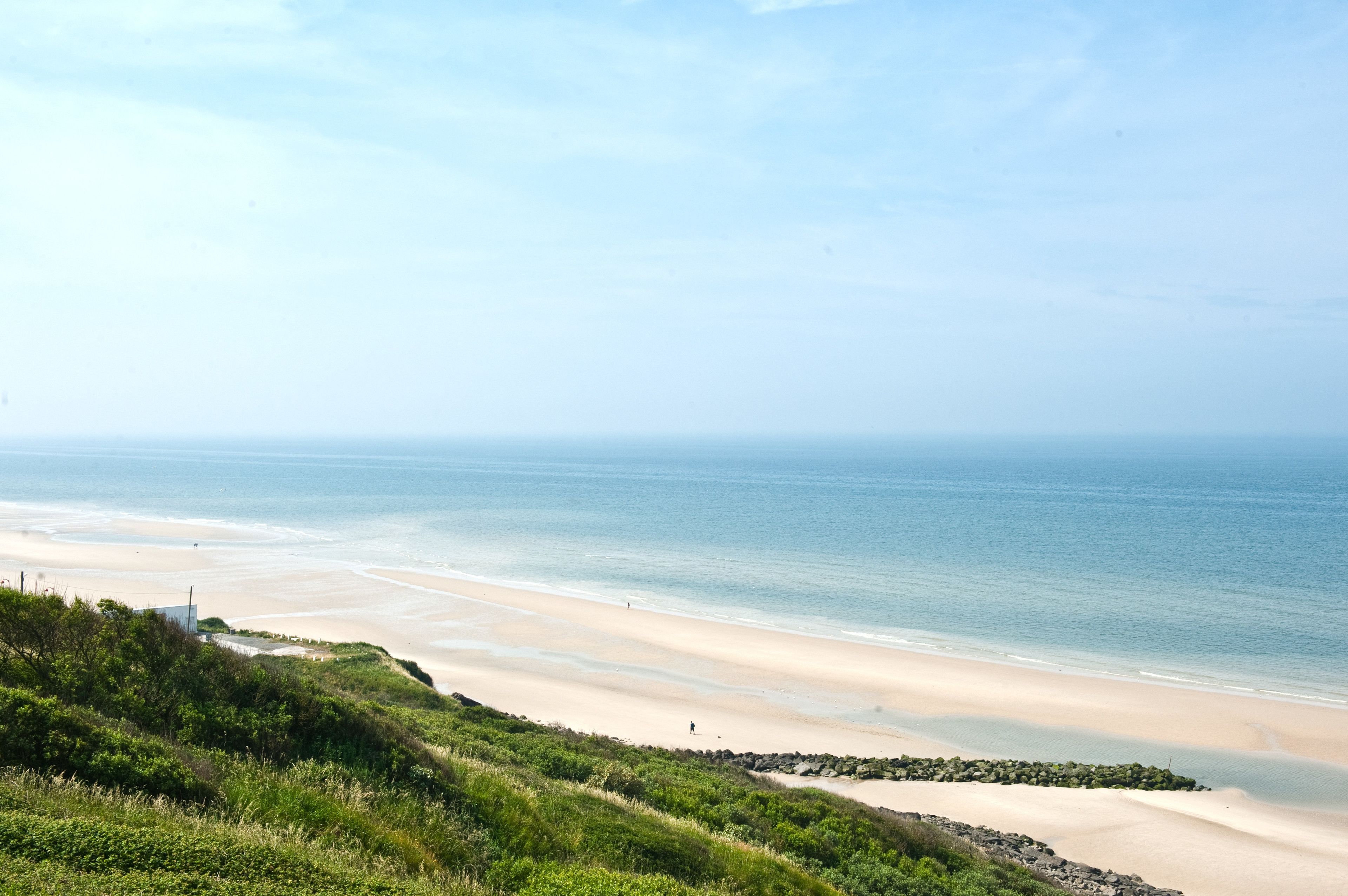 Ett kustlandskap med en sandstrand, gräsbeklädda kullar och en klar himmel.