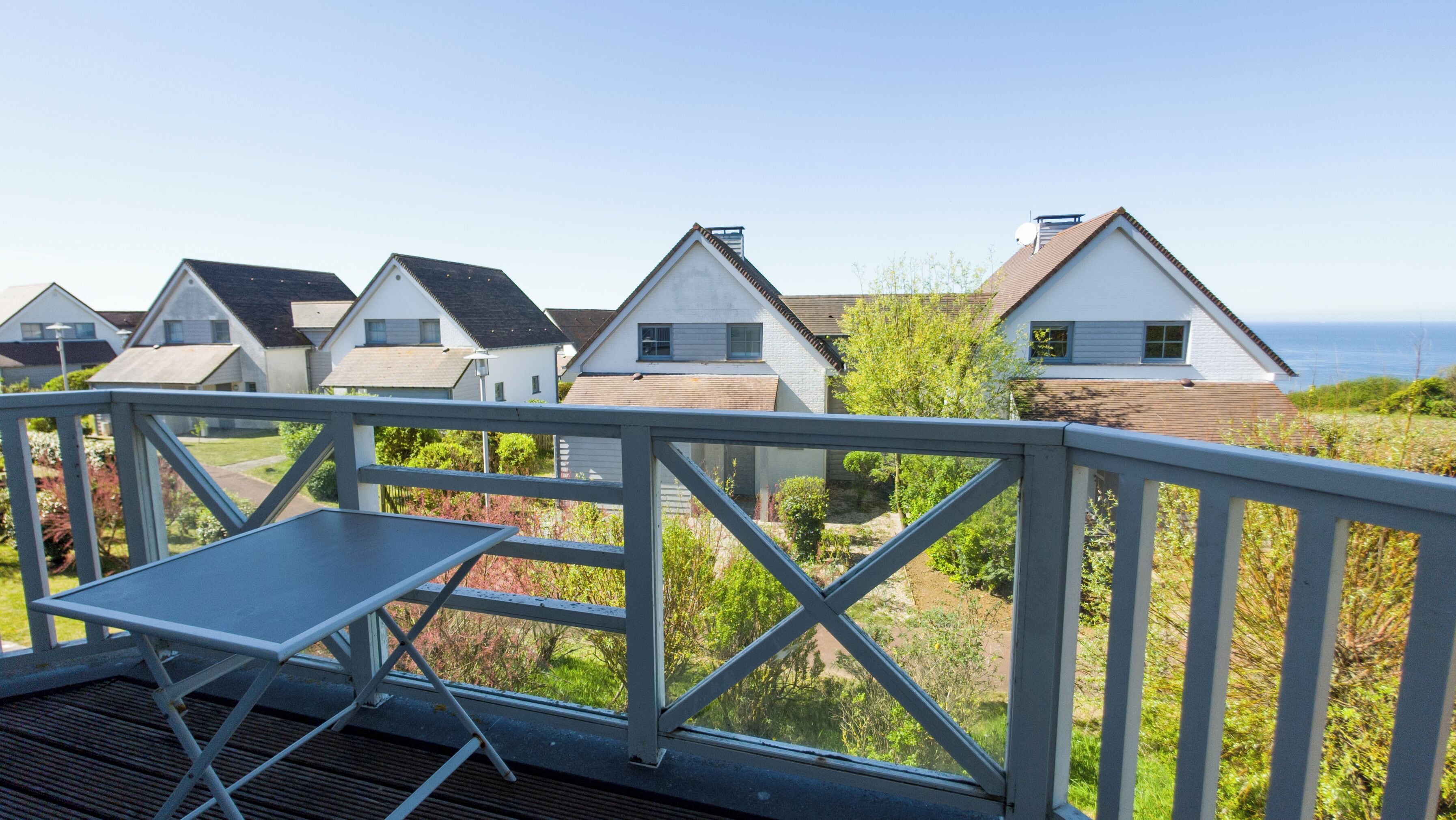 A coastal residential area with multiple houses, a deck with a table, and a view of the sea.