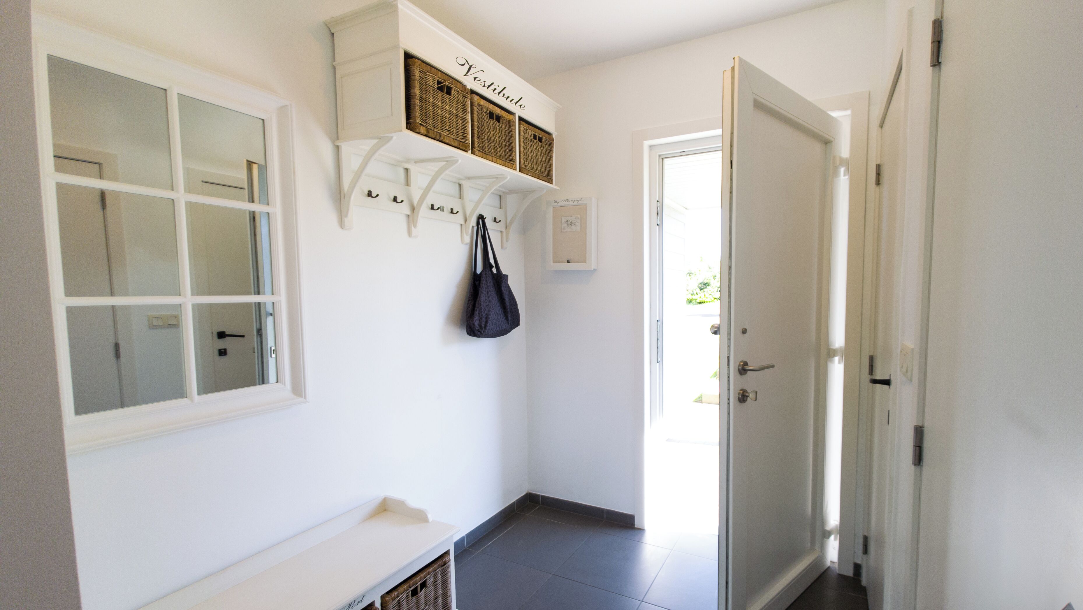 A hallway with a white bench, a door, and a wall-mounted basket rack with baskets.