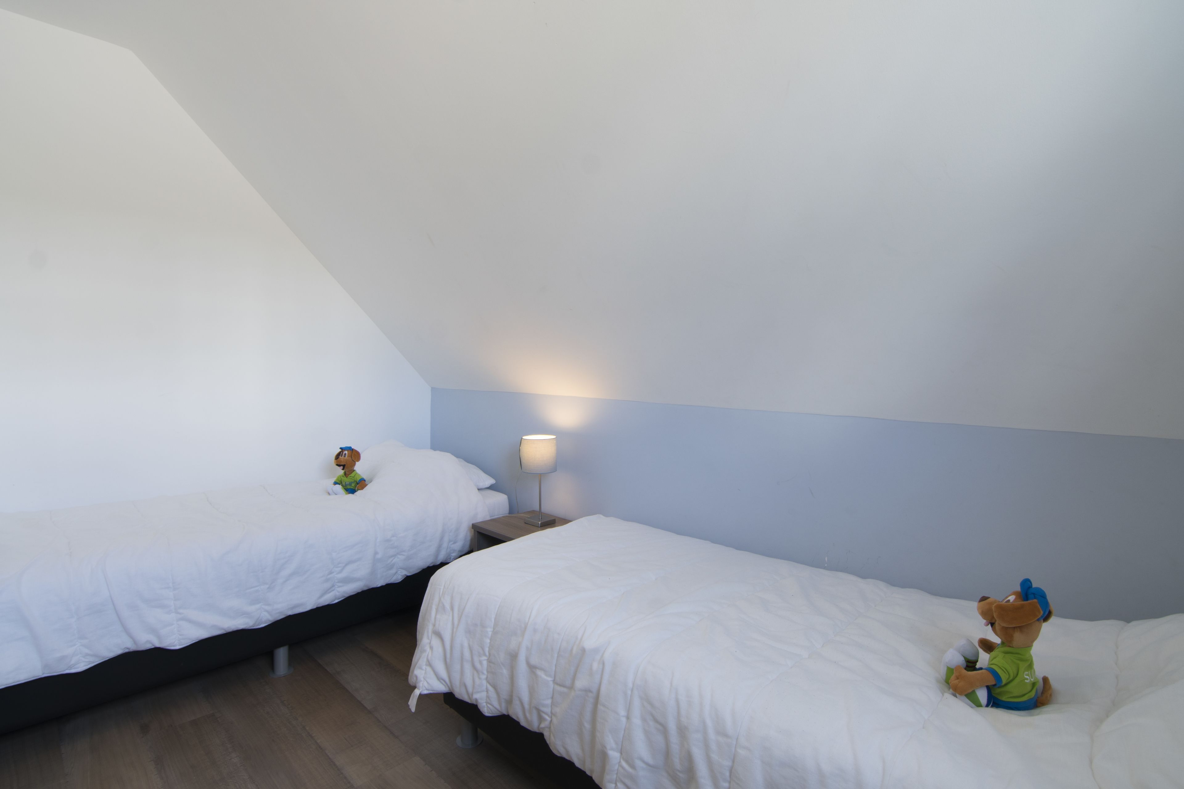 Una habitación con dos camas individuales, una mesita de noche con lámpara y una figurita sobre una de las camas.