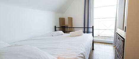 Una camera da letto con due letti, una finestra con tende e un termosifone.