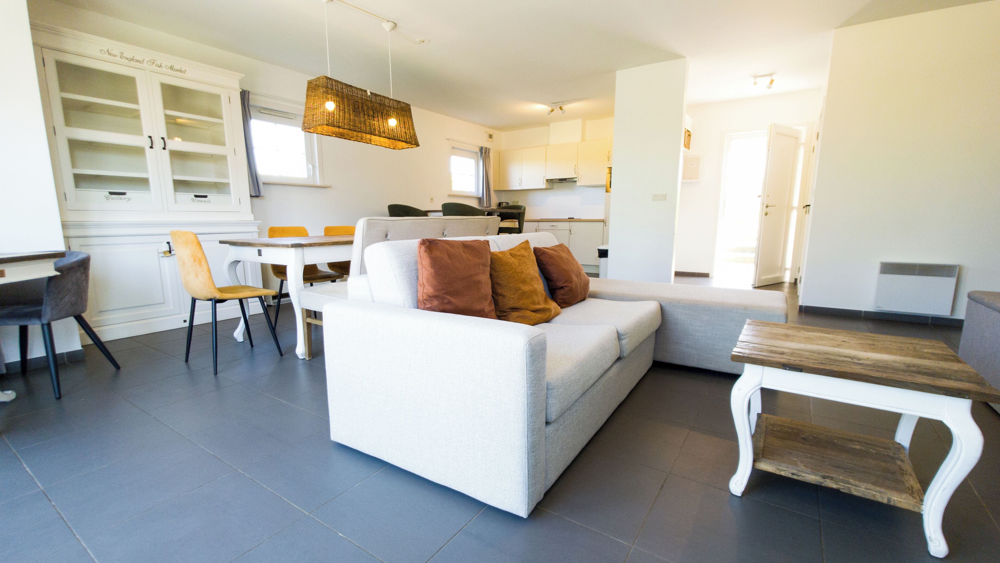 A modern living room with a sofa, a dining table, and chairs. There is a kitchen area in the background.