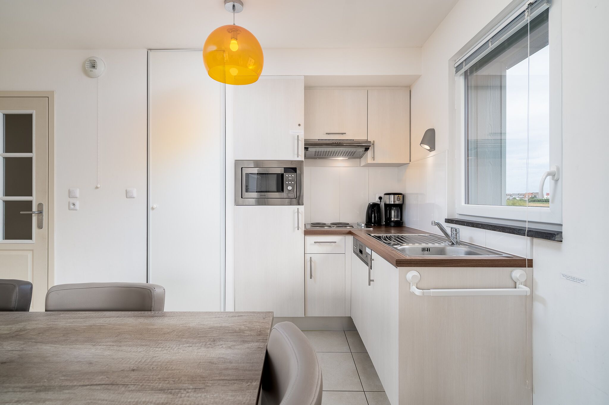A modern kitchen with white cabinets, a stainless steel microwave, a coffee maker, and a window overlooking the city.
