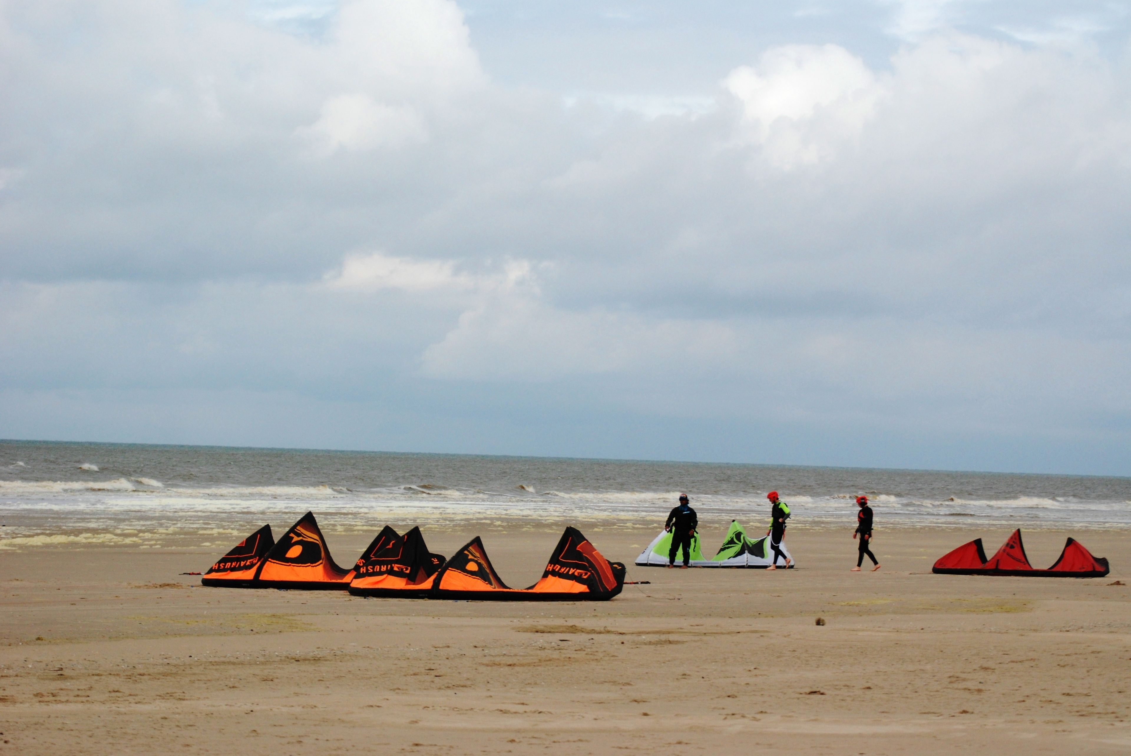 A beach with several kites and people walking.