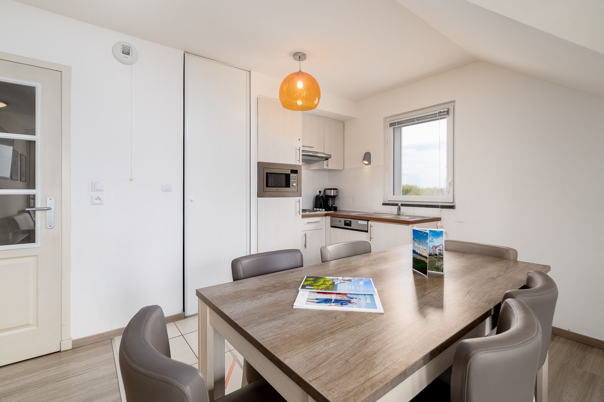 A modern kitchen with white cabinets, a wooden dining table, and a hanging pendant light.