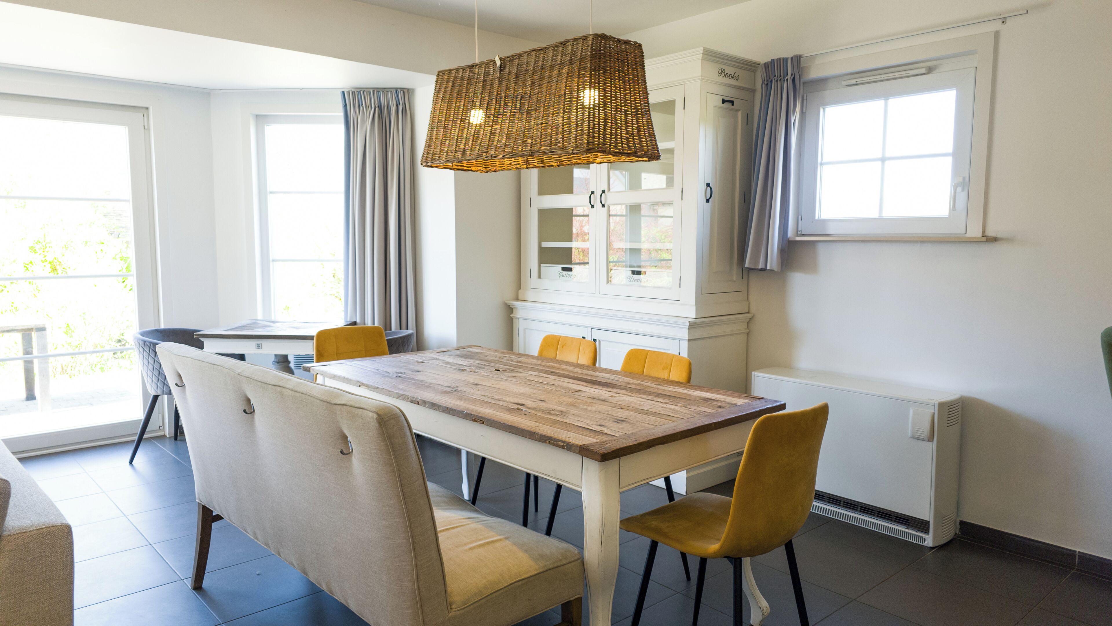 Un coin repas comprenant une table en bois, des chaises, un luminaire suspendu et un meuble avec des portes en verre.