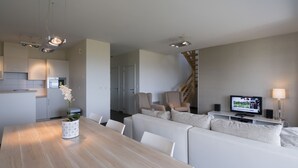 Una sala de estar moderna con una mesa de comedor de madera, sofás blancos, un televisor y una escalera.