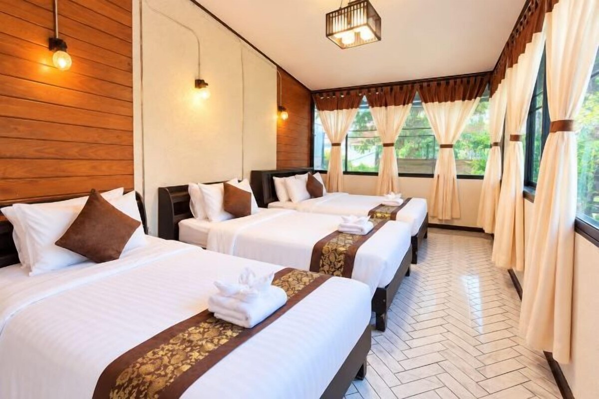 Habitación de hotel con tres camas, paredes de madera y ventanas amplias con cortinas.