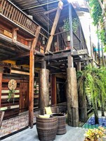 Un edificio rústico de madera con un balcón, grandes columnas de madera y asientos al aire libre.