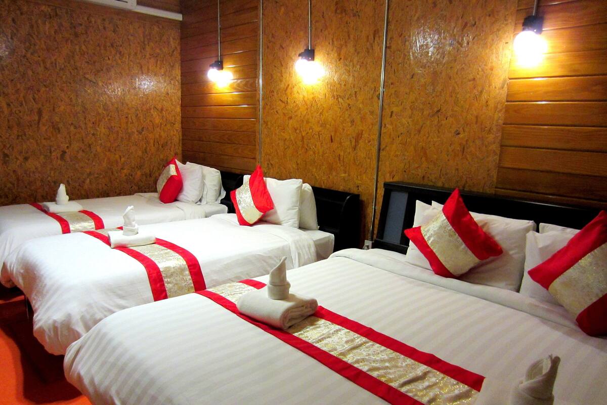 Quarto de hotel com duas camas, cada uma com roupa de cama branca e detalhes vermelhos, e uma parede de madeira.