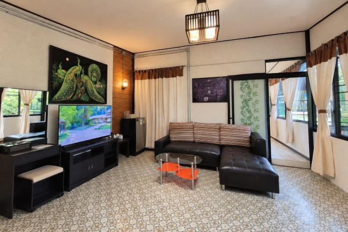 Una sala de estar moderna con un televisor de pantalla plana, un sofá de cuero negro, una mesa de centro de vidrio y un ventanal con cortinas.
