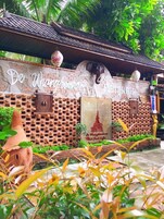 Un edificio tailandés tradicional con un muro de ladrillo, una gran estatua de Buda y un letrero que dice "De Wangkumkam".