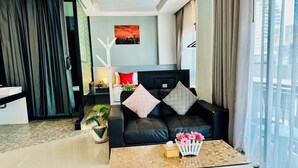 A modern living room with a black sofa, a coffee table, and a cityscape painting on the wall. - PJ Patong Resortel (Patong)