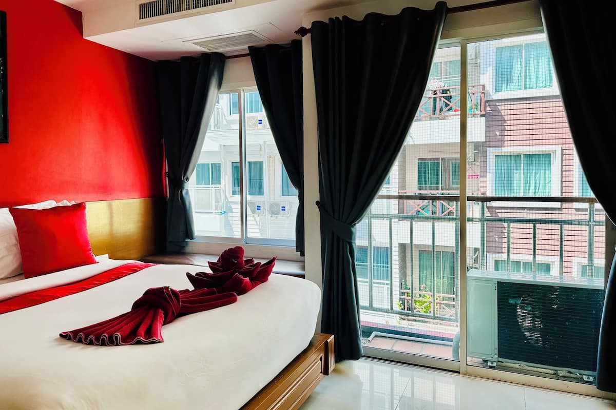 A hotel room with a large bed, red walls, and a view of a building through the window.