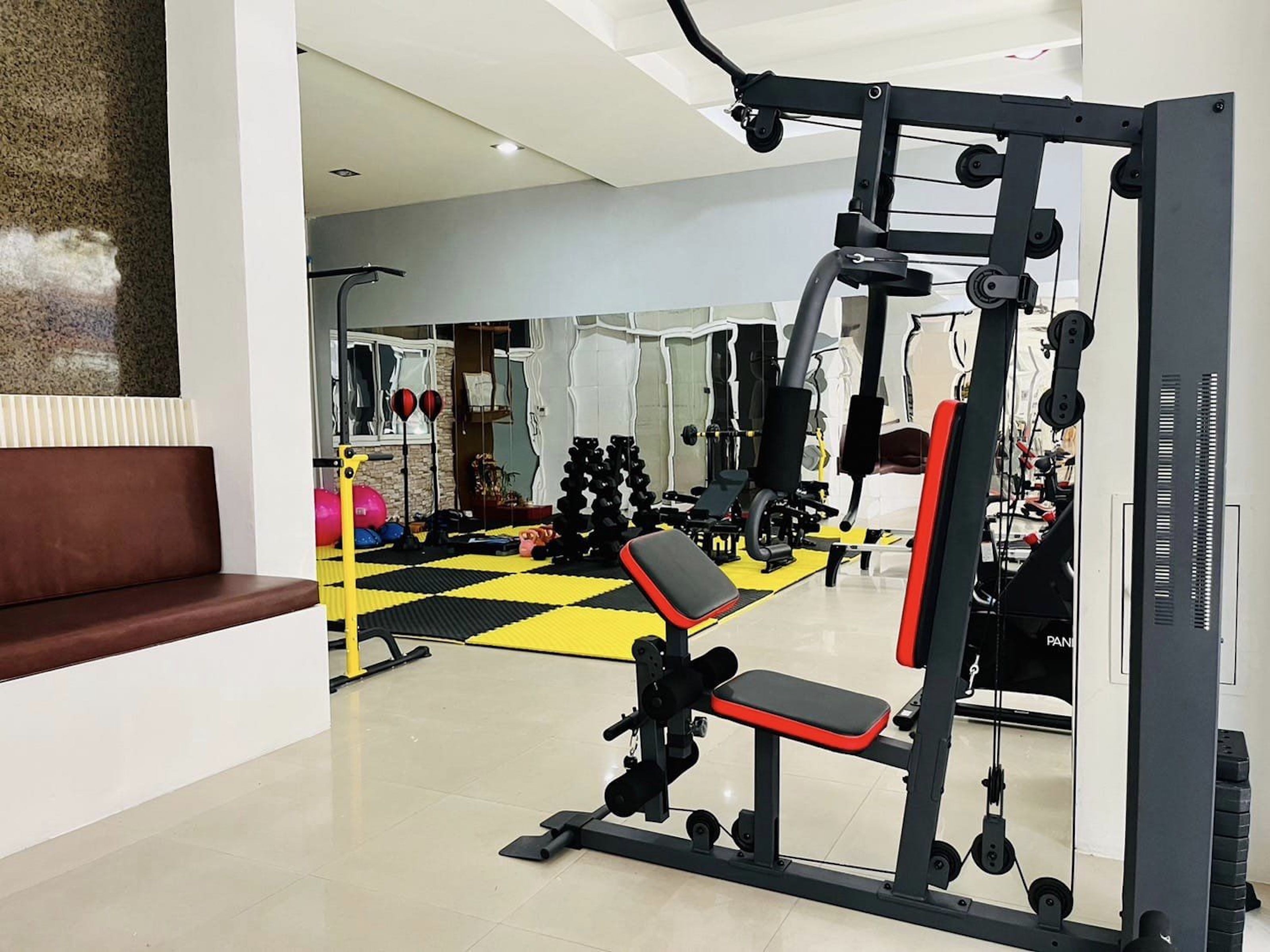 A gym with a bench, weight machines, and a mirrored wall.