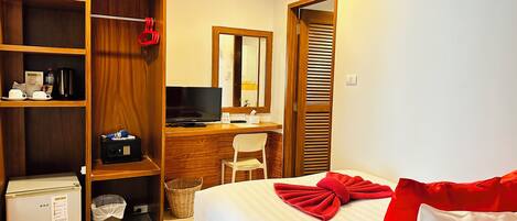 A hotel room with a bed, a desk with a computer, a mini fridge, a wardrobe, and a trash bin.
