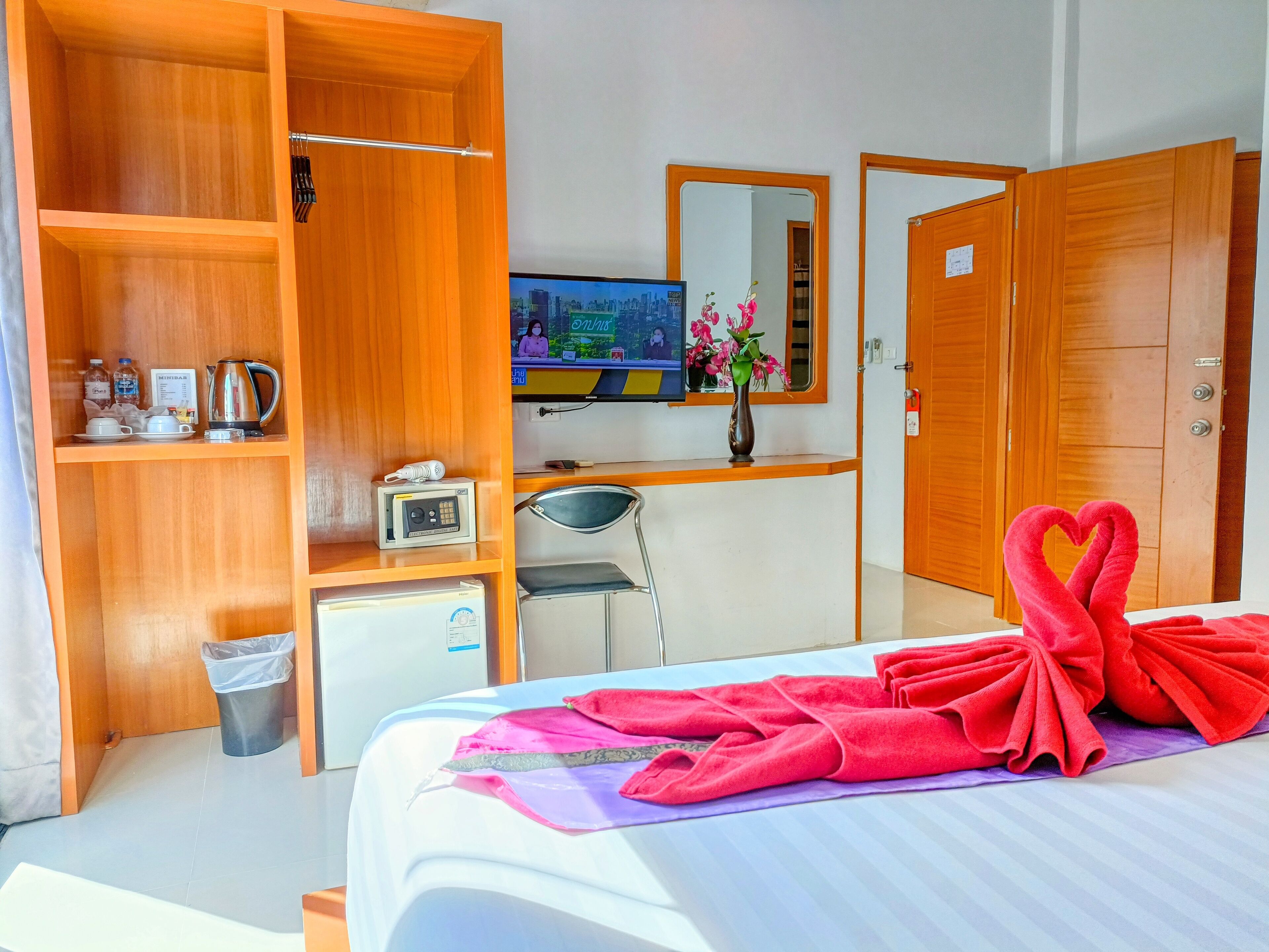 A hotel room with a bed, a desk with a computer, a TV, a wardrobe, and a trash bin.