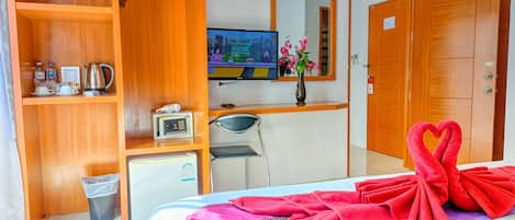 A hotel room with a bed, a desk with a computer, a TV, a wardrobe, and a trash bin.