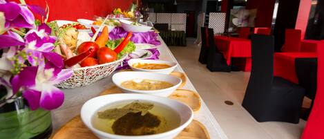 A buffet setup with various dishes and a decorative vase of purple flowers.