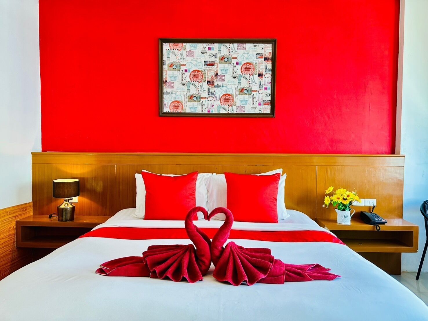 Habitación de hotel con una decoración en tonos rojo y blanco, una cama con almohadas rojas, un cuadro en la pared y una decoración de toalla con forma de cisne sobre la cama.