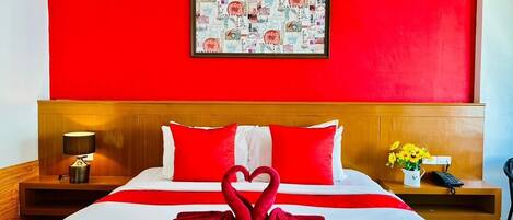 Habitación de hotel con una decoración en tonos rojo y blanco, una cama con almohadas rojas, un cuadro en la pared y una decoración de toalla con forma de cisne sobre la cama.