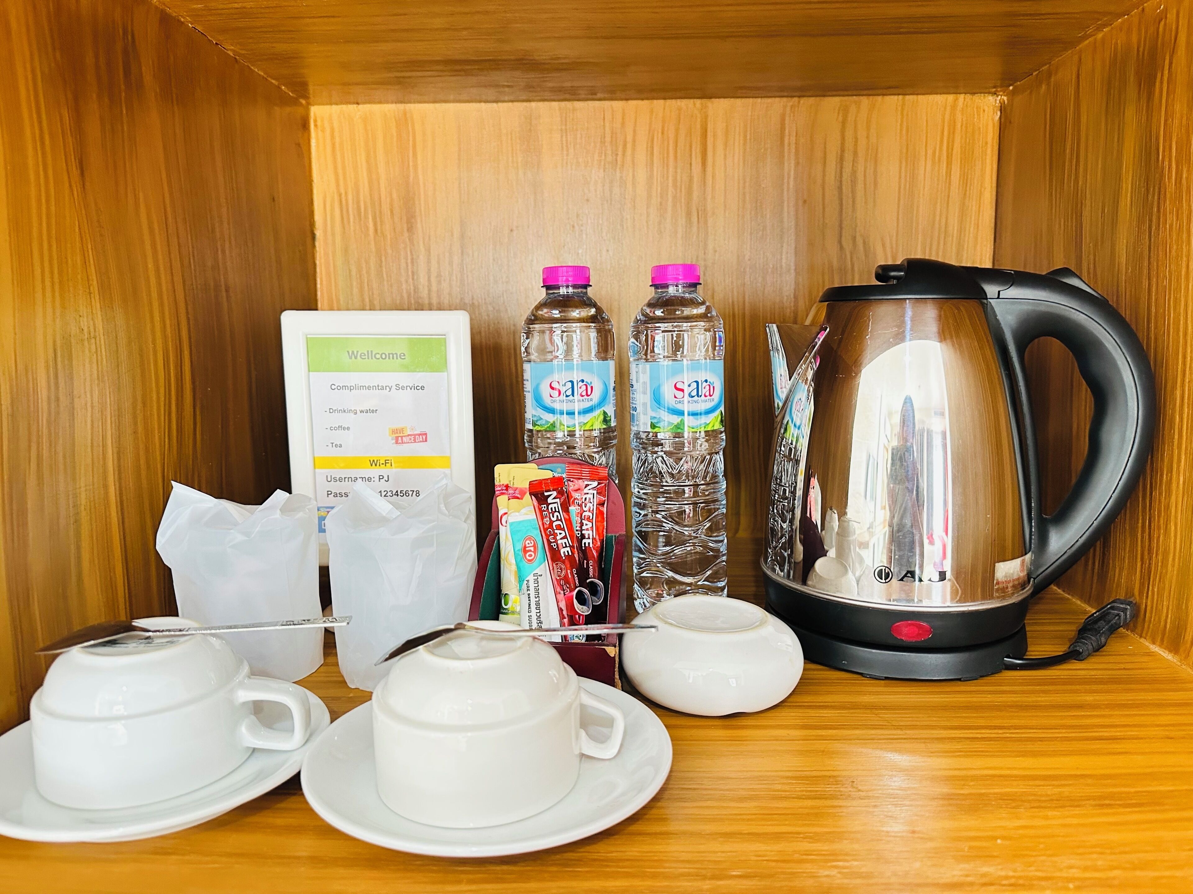 Dans une chambre d’hôtel, on trouve un plateau de petit-déjeuner avec une machine à café, deux bouteilles d’eau, un sachet de thé, un sachet de café Nescafé et un panneau indiquant la disponibilité du Wi-Fi.
