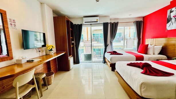 A hotel room with a desk, two beds, a TV, and a balcony with curtains. - PJ Patong Resortel (Patong)