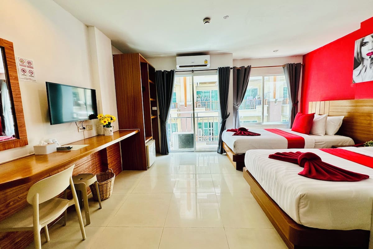 A hotel room with a desk, two beds, a TV, and a balcony with curtains.