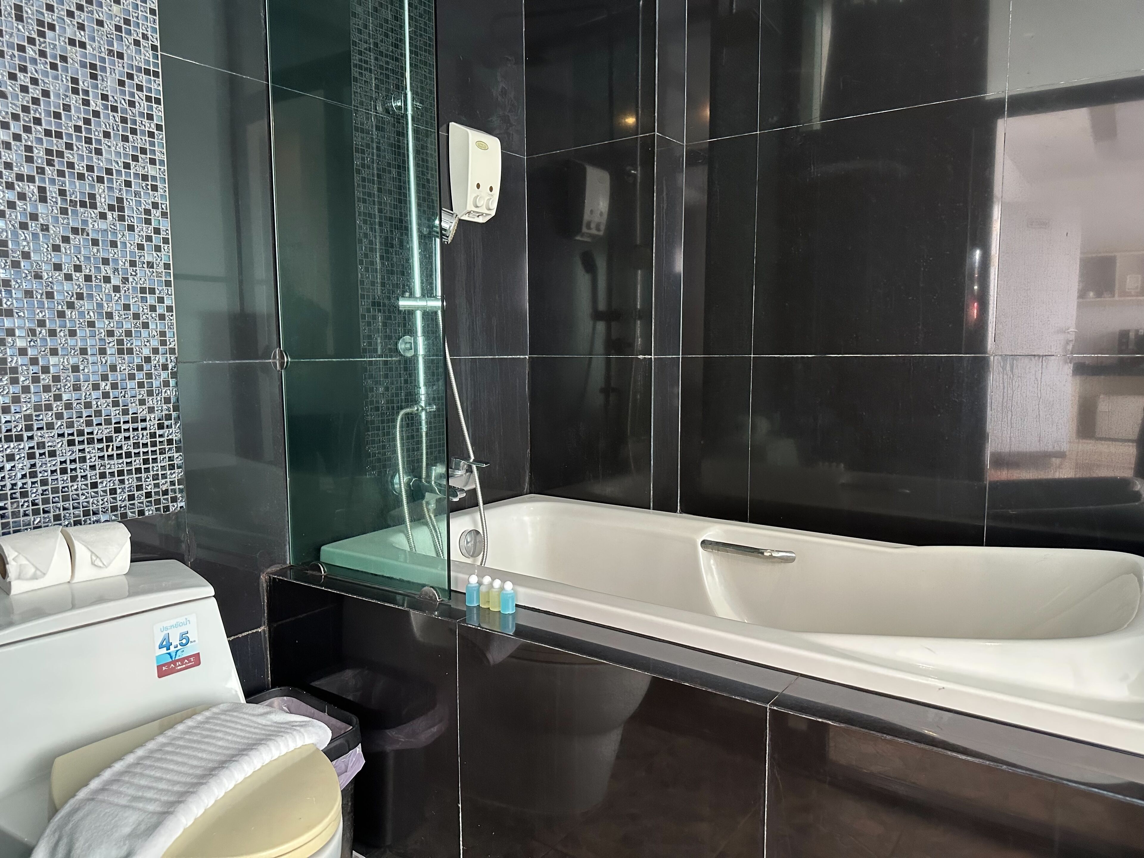 Un baño moderno con ducha envuelta en vidrio, una bañera blanca y un inodoro con toalla blanca.