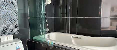 A modern bathroom with a glass-enclosed shower, a white bathtub, and a toilet with a white towel.