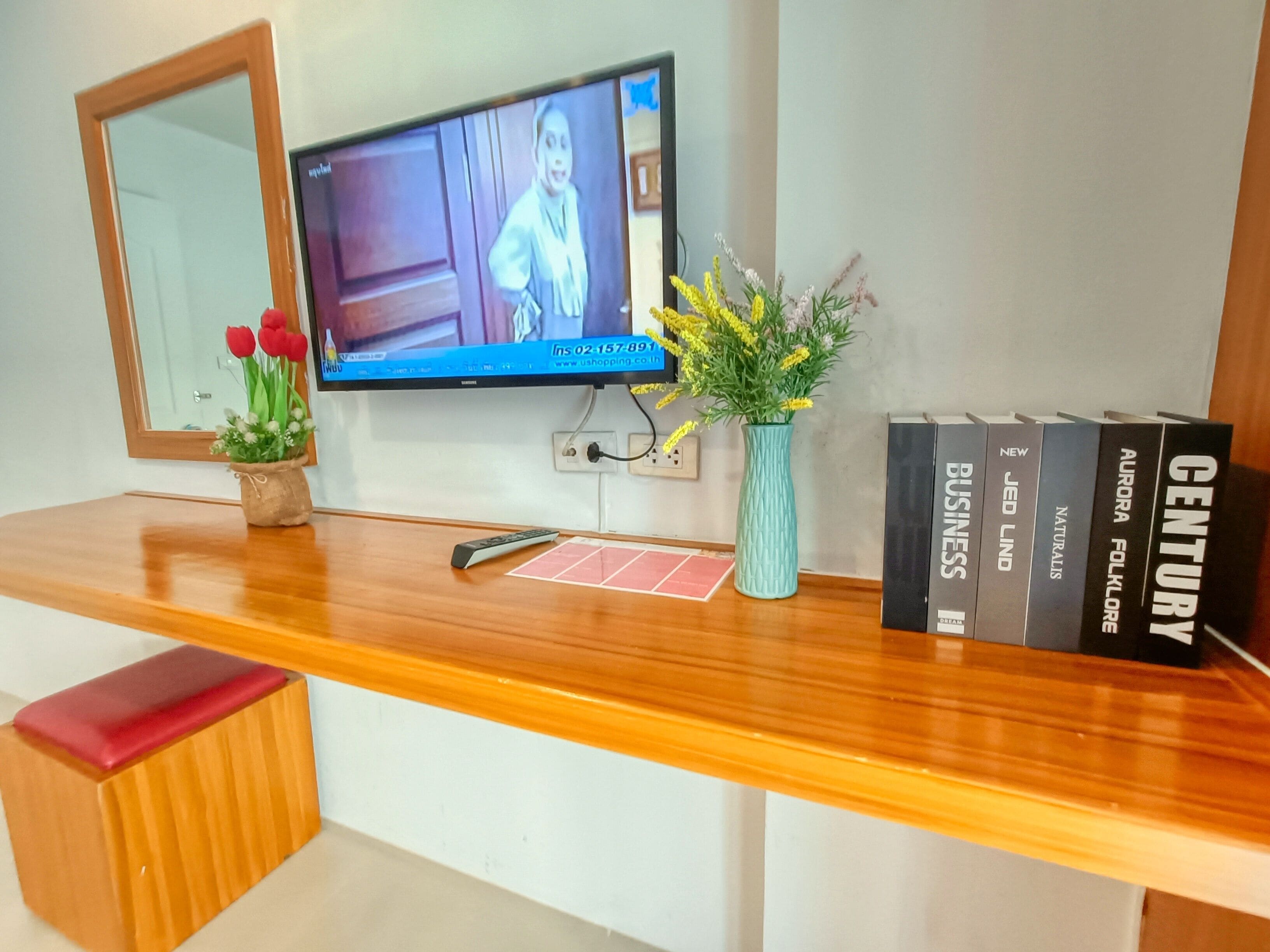 Un mostrador de recepción de madera con un televisor, un florero con flores, un control remoto y una hilera de libros.