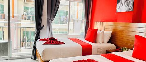 Une chambre d’hôtel avec deux lits, un mur d’accent rouge et une grande fenêtre avec des rideaux.