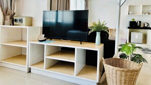 A modern living room with a flat-screen TV on a wooden TV stand, a small table with a vase of flowers, and a wicker basket. - PJ Patong Resortel (Patong)