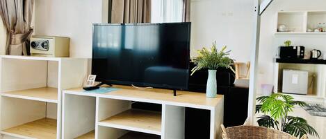 A modern living room with a flat-screen TV on a wooden TV stand, a small table with a vase of flowers, and a wicker basket.