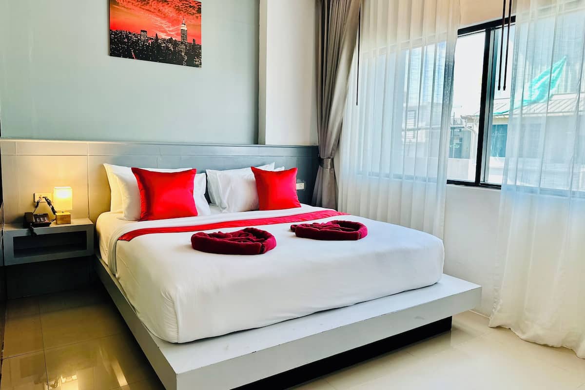 A hotel room with a large bed, a nightstand with a lamp, and a cityscape painting on the wall.